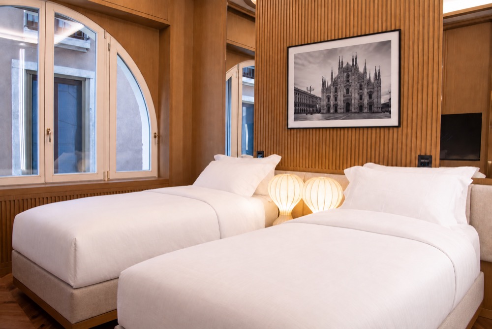 Twin bedroom with two single beds, two lamps, a photograph of the Duomo and an arched window